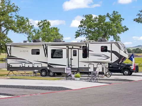 Fifth-wheel trailer with patio chairs and a Texas flag beneath live oaks at Lantern Oaks