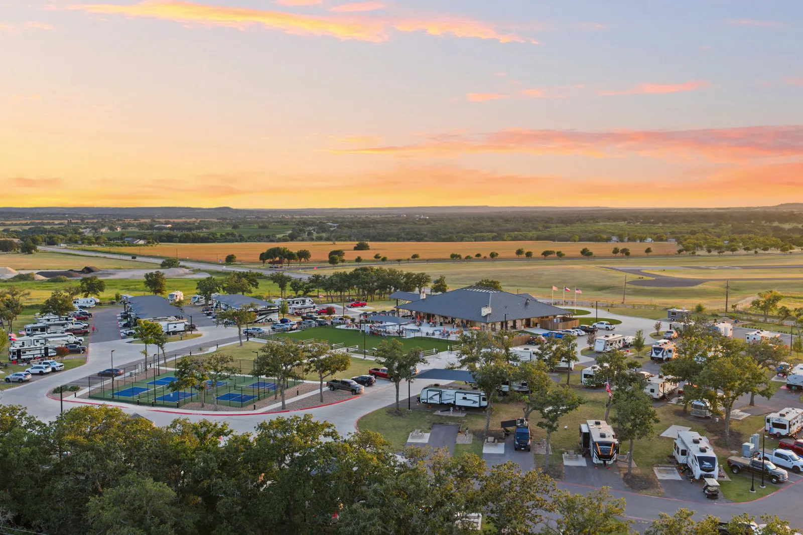 Aerial view of Lantern Oaks RV Resort at sunset, with RV sites, pickleball courts and the Hill Country beyond